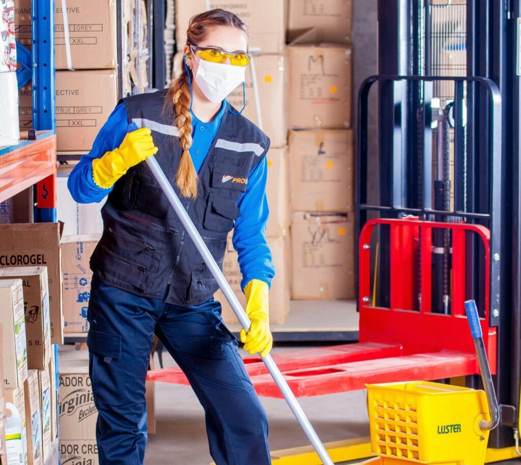 pexels-photo-209271-209271 Female janitor in safety gear cleaning a warehouse floor with a mop and bucket.